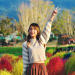 Asian woman in a striped sweater making a peace sign in a colorful field in South Korea.