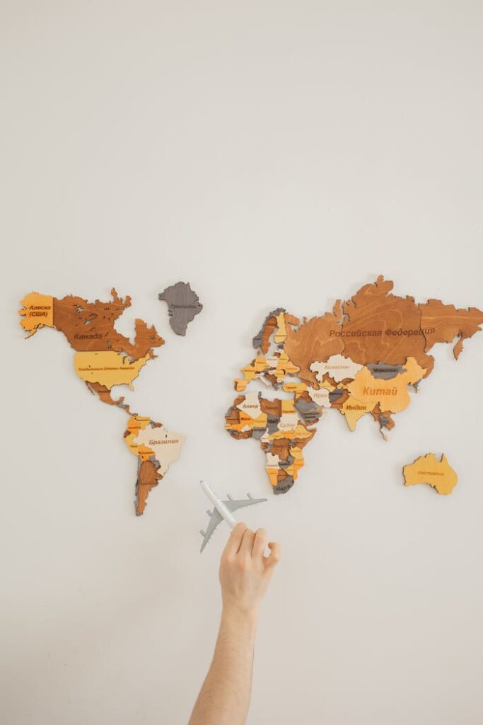 A hand holding a toy plane points to a colorful decorative world map on a wall.